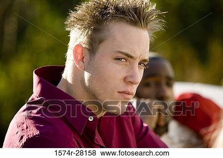 Stock Photo - Portrait of a young man staring while other sitting in background. Fotosearch