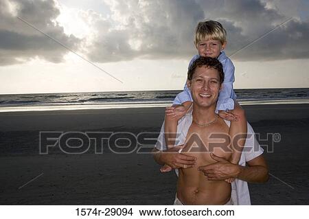 Portrait of a young man with son on shoulders at the beach View Large Photo Image Picture - Portrait of a young man with son on shoulders at the beach. Fotosearch