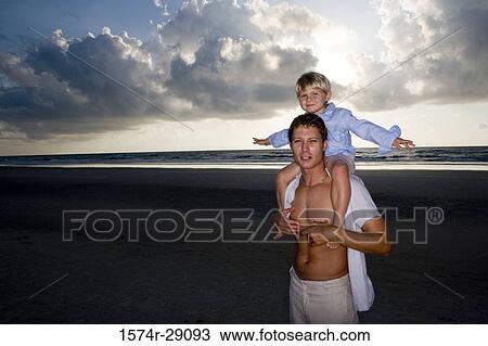 Stock Image - Portrait of a young man with son on shoulders at the beach. Fotosearch