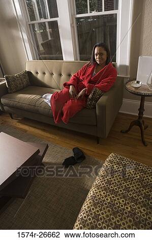 Stock Image - Portrait of a young woman in gown sitting on a sofa. Fotosearch