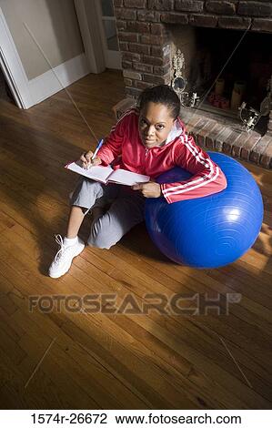 Portrait of a young woman in sports clothing writing in a book by fitness ball View Large Photo Image Stock Image - Portrait of a young woman in sports clothing writing in a book by fitness ball. Fotosearch