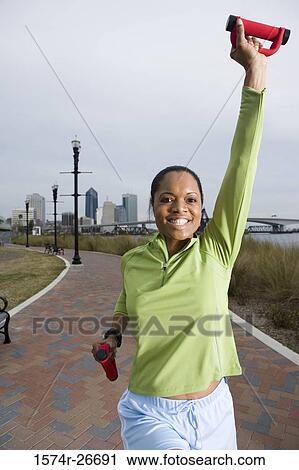 Stock Image - Portrait of a young woman in sports clothing jogging on walkway. Fotosearch