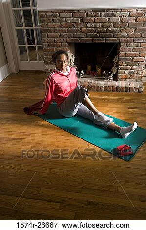 Stock Photo - Portrait of a young woman in sports clothing exercising on mat by fire place. Fotosearch