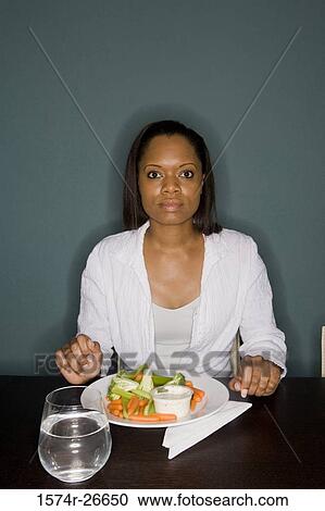 Portrait of a young woman sitting by table with a plate of vegetables View Large Photo Image Stock Image - Portrait of a young woman sitting by table with a plate of vegetables. Fotosearch