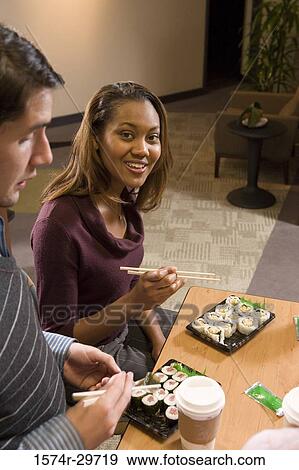 Stock Photo - Portrait of a young woman sitting by table and holding chop sticks. Fotosearch