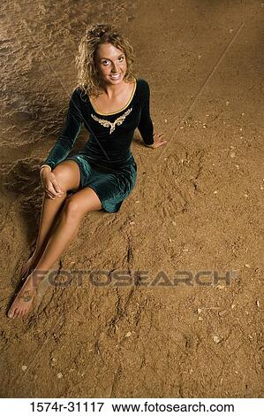 Stock Photo - Portrait of a young woman sitting on sand. Fotosearch