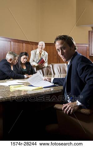 Portrait of businessman sitting by conference table while colleagues discussing in the background View Large Photo Image Picture - Portrait of businessman sitting by conference table while colleagues discussing in the background. Fotosearch
