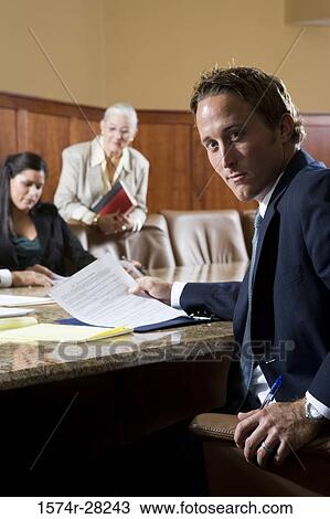 Portrait of businessman sitting by conference table while businesswomen in background View Large Photo Image Stock Image - Portrait of businessman sitting by conference table while businesswomen in background. Fotosearch