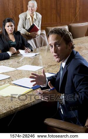 Stock Photograph - Portrait of businessman sitting by conference table while colleagues discussing in the background. Fotosearch