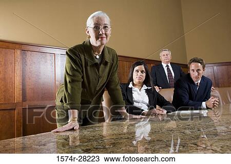 Stock Image - Portrait of businesswoman leaning on conference table while colleagues beside her. Fotosearch