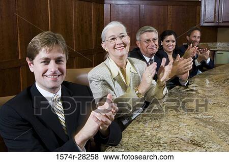 Stock Photo - Portrait of cheerful business people sitting by conference table and applauding in an office. Fotosearch