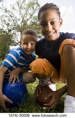Stock Photo - Portrait of cheerful children standing with footballs at park. Fotosearch