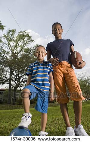 Stock Photograph - Portrait of cheerful children standing with footballs at park. Fotosearch