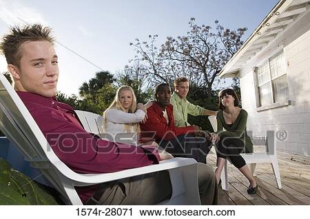Portrait of cheerful friends sitting on armchairs on wooden deck View Large Photo Image Stock Image - Portrait of cheerful friends sitting on armchairs on wooden deck. Fotosearch