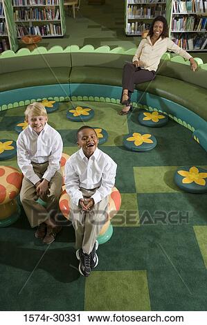 Portrait of cheerful schoolboys sitting on stools while teacher sitting on sofa View Large Photo Image Stock Image - Portrait of cheerful schoolboys sitting on stools while teacher sitting on sofa. Fotosearch