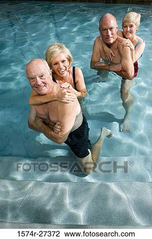 Stock Image - Portrait of cheerful senior couples embracing in swimming pool. Fotosearch
