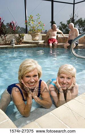 Portrait of cheerful senior women lying in swimming pool while senior men discussing in the background View Large Photo Image Stock Photography - Portrait of cheerful senior women lying in swimming pool while senior men discussing in the background. Fotosearch