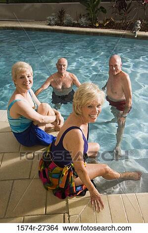 Picture - Portrait of cheerful senior women sitting poolside while senior men in swimming pool. Fotosearch
