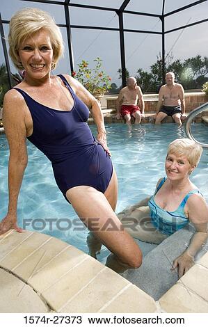 Stock Image - Portrait of cheerful senior women poolside while senior men sitting in the background. Fotosearch