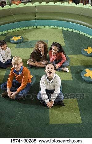 Stock Photo - Portrait of cheerful students sitting on floor in the library. Fotosearch