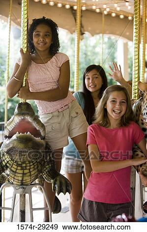Stock Photo - Portrait of cheerful teenage girls standing on a carousel. Fotosearch