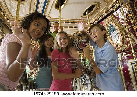 Stock Image - Portrait of cheerful teenagers standing in a carousel and waving hand. Fotosearch