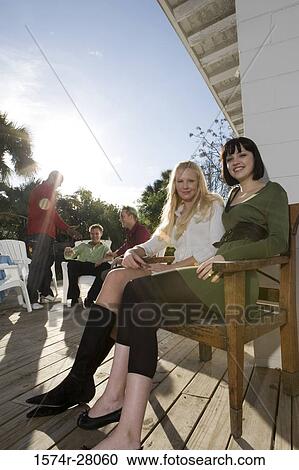 Portrait of cheerful women sitting on armchairs while men discussing in background View Large Photo Image Stock Image - Portrait of cheerful women sitting on armchairs while men discussing in background. Fotosearch