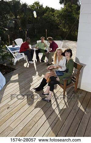 Portrait of cheerful women sitting on armchairs while men discussing in background View Large Photo Image Stock Photo - Portrait of cheerful women sitting on armchairs while men discussing in background. Fotosearch