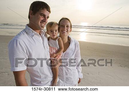 Stock Image - Portrait of cheerful young couple with daughter on the beach. Fotosearch
