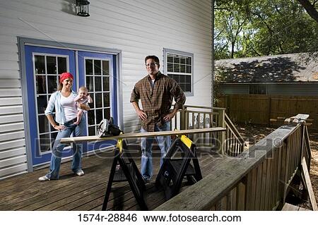 Stock Photograph - Portrait of cheerful young family standing with hand on hip. Fotosearch