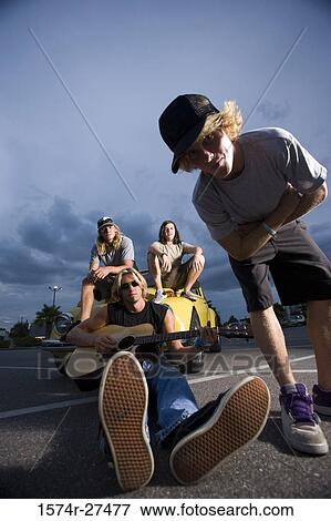 Stock Photo - Portrait of friends enjoying music by a car at the parking area. Fotosearch