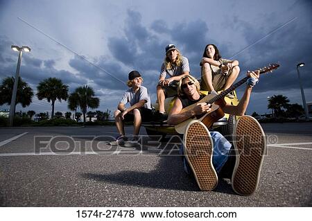 Stock Photo - Portrait of friends enjoying music by a car at the parking area. Fotosearch