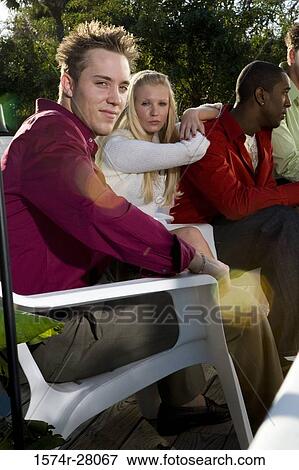 Stock Photo - Portrait of friends sitting on armchairs on wooden deck. Fotosearch