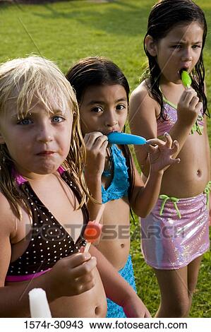 Stock Image - Portrait of girls standing together and eating flavored ice. Fotosearch