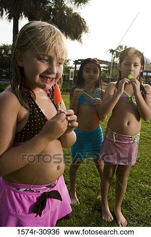 Stock Photograph - Portrait of girls standing together and eating flavored ice. Fotosearch