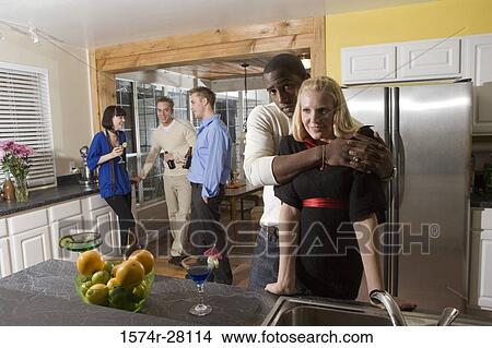 Picture - Portrait of man embracing woman in domestic kitchen while their friends standing in background. Fotosearch
