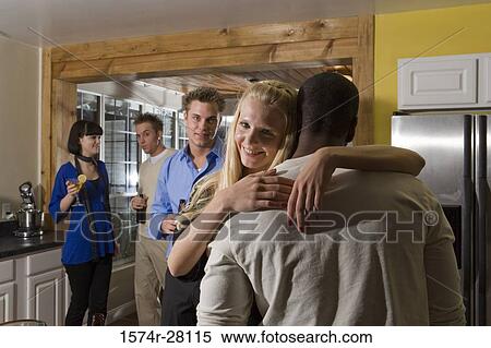 Portrait of man embracing woman in domestic kitchen while friends standing in background View Large Photo Image Stock Photography - Portrait of man embracing woman in domestic kitchen while friends standing in background. Fotosearch