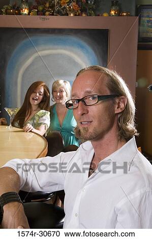 Stock Image - Portrait of mature man sitting by bar counter while wife and daughter behind. Fotosearch
