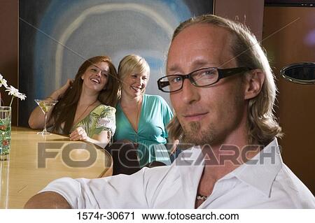 Stock Image - Portrait of mature man sitting by bar counter while wife and daughter behind. Fotosearch