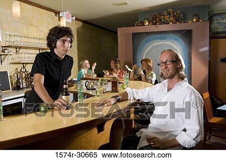 Portrait of mature man sitting by bar counter with family members around View Large Photo Image Stock Photography - Portrait of mature man sitting by bar counter with family members around. Fotosearch