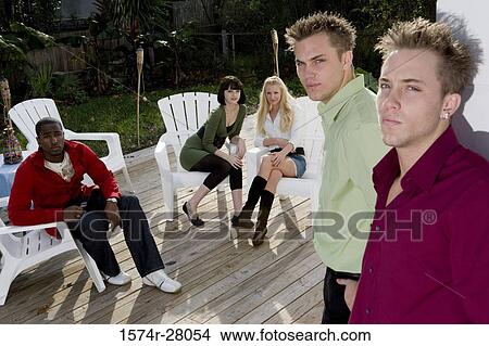 Portrait of men leaning by wall while friends sitting on armchairs in background View Large Photo Image Picture - Portrait of men leaning by wall while friends sitting on armchairs in background. Fotosearch