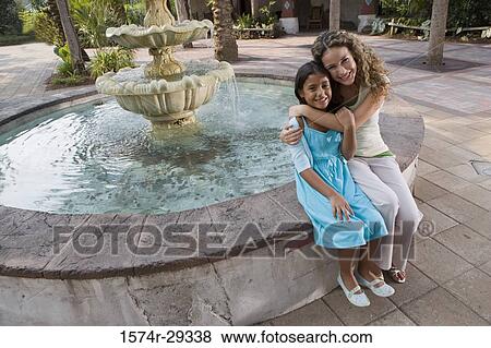 Portrait of mother and daughter sitting together by water fountain View Large Photo Image Stock Photo - Portrait of mother and daughter sitting together by water fountain. Fotosearch