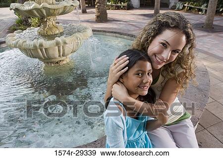 Portrait of mother and daughter sitting together by water fountain View Large Photo Image Stock Photo - Portrait of mother and daughter sitting together by water fountain. Fotosearch