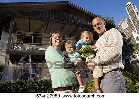 Stock Photo - Portrait of parents holding their children in front of a house. Fotosearch