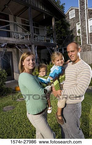 Stock Photograph - Portrait of parents holding their children in front of a house. Fotosearch