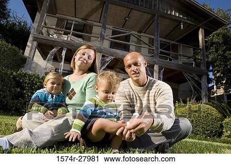 Stock Image - Portrait of parents sitting with their children in front of a house. Fotosearch