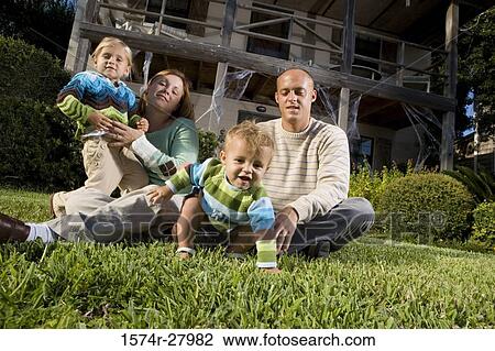 Stock Image - Portrait of parents sitting with their children in front of a house. Fotosearch