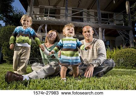 Stock Image - Portrait of parents sitting with their children in front of a house. Fotosearch