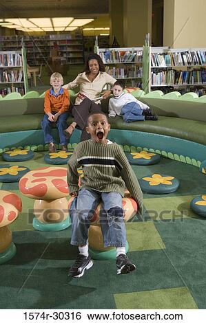Stock Photograph - Portrait of schoolboys and teacher sitting in library. Fotosearch