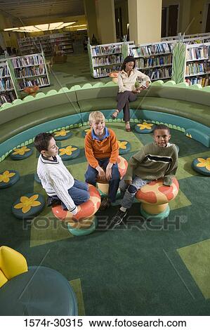 Portrait of schoolboys sitting on stools while teacher reading book in the library View Large Photo Image Stock Photography - Portrait of schoolboys sitting on stools while teacher reading book in the library. Fotosearch